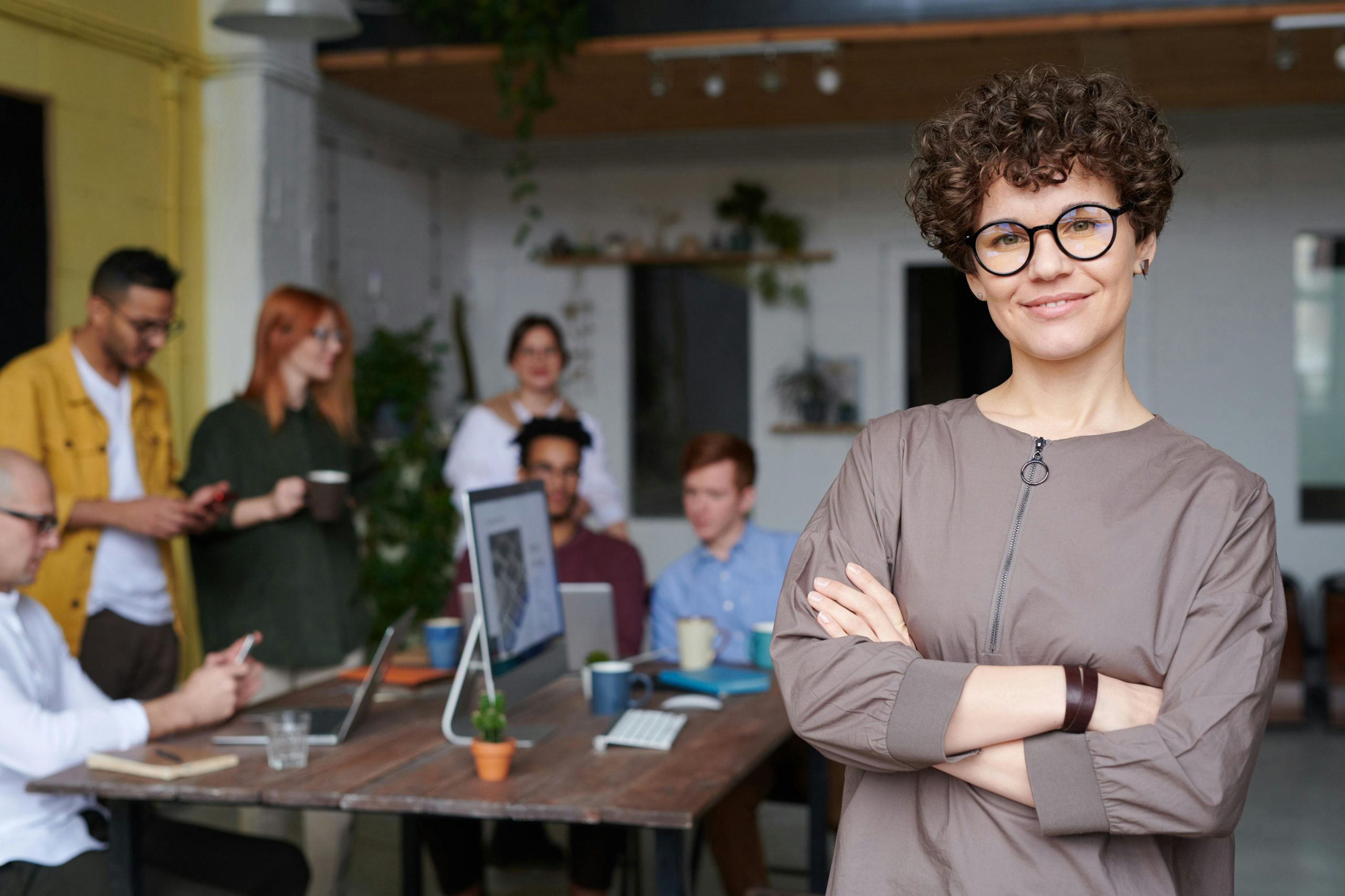 smiling manager with arms crossed, standing near a group of employees who are talking casually